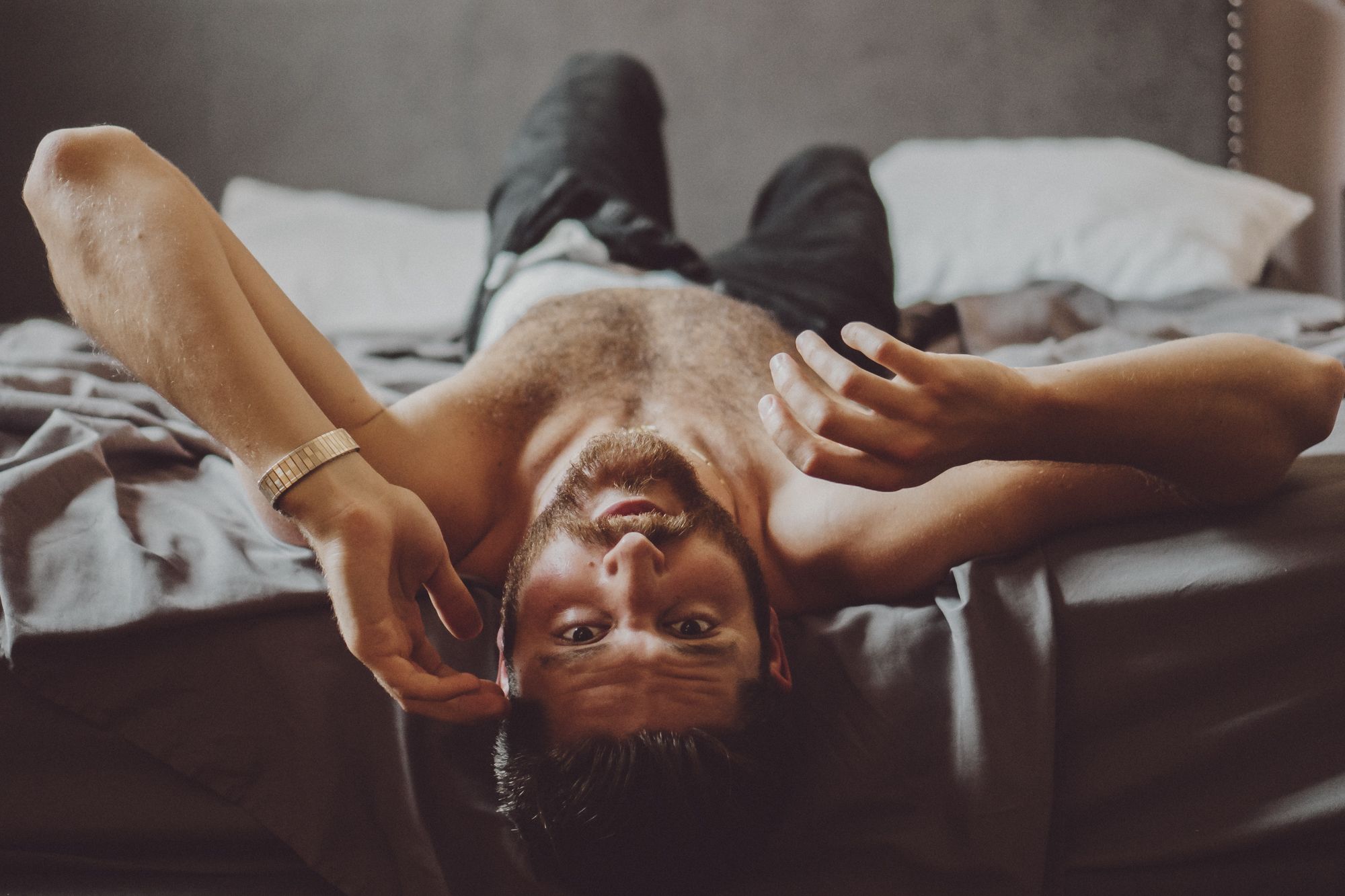 Handsome and rugged man lays seductively on a bed, shirtless with undone jeans