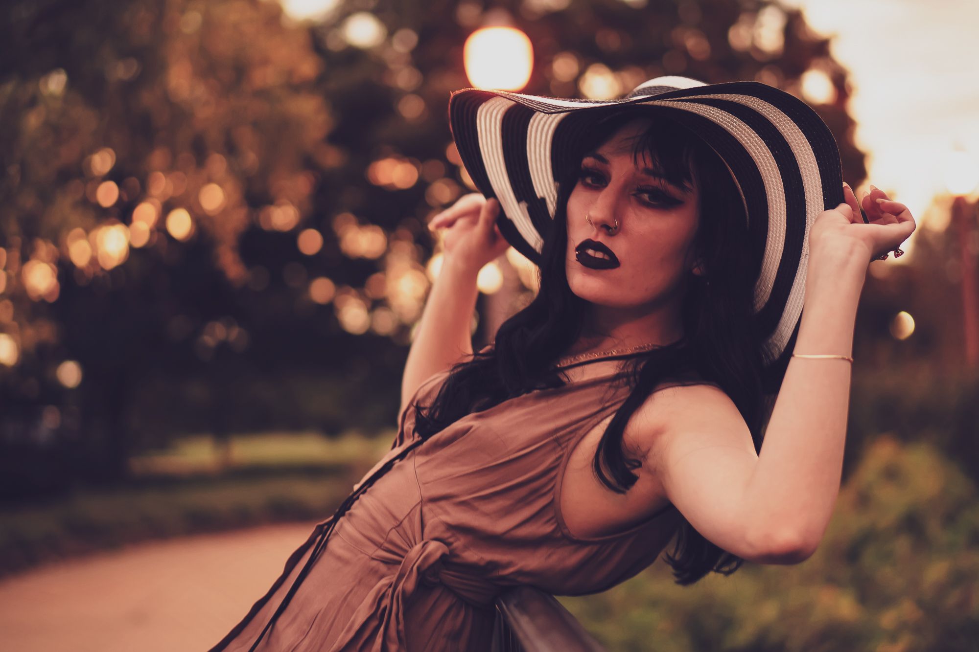 Dark and mysterious model drapes across the railing of a bridge in her wide brimmed hat in the dark and moody boho scene