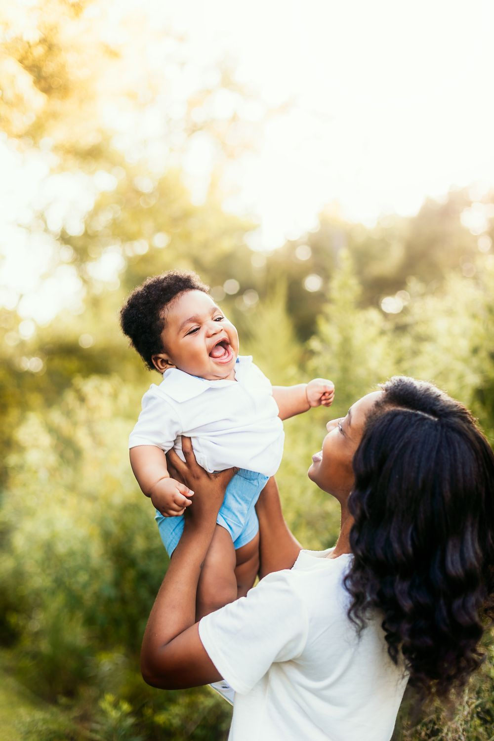 Parent lifting laughing child in white shirt against golden sunset bokeh background.