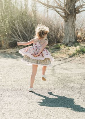 Young girl in floral dress twirling joyfully on a sunlit path near bare winter trees.