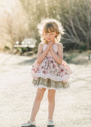 Little girl in floral layered dress standing in golden sunlight on a country path.