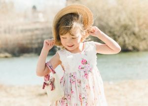 Happy young girl in floral dress and straw hat smiling outdoors near a sunny river.