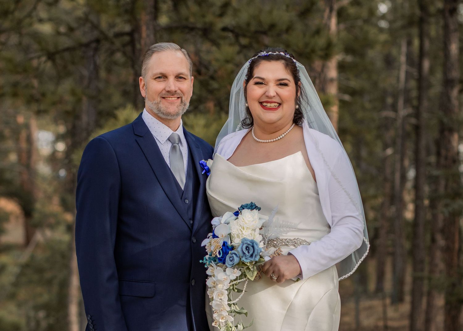 Bride and groom pose for romantic winter wedding photos in a wooded forest setting with blue floral bouquet in Garden of the Gods, CO, USA.
