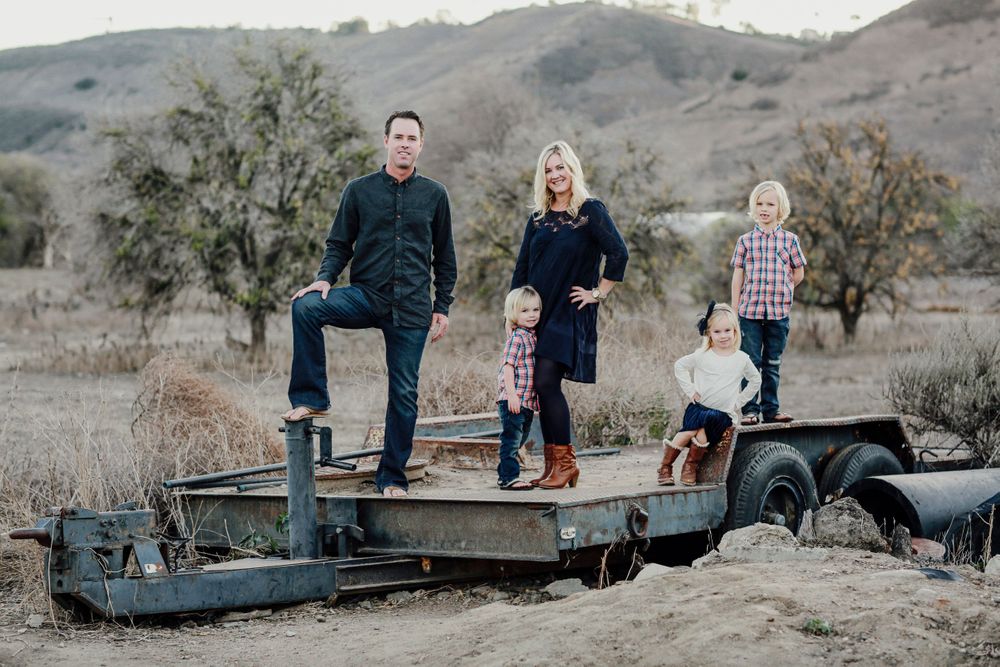 A family stands together on an old rustic flatbed trailer in a rural hillside setting during golden hour.