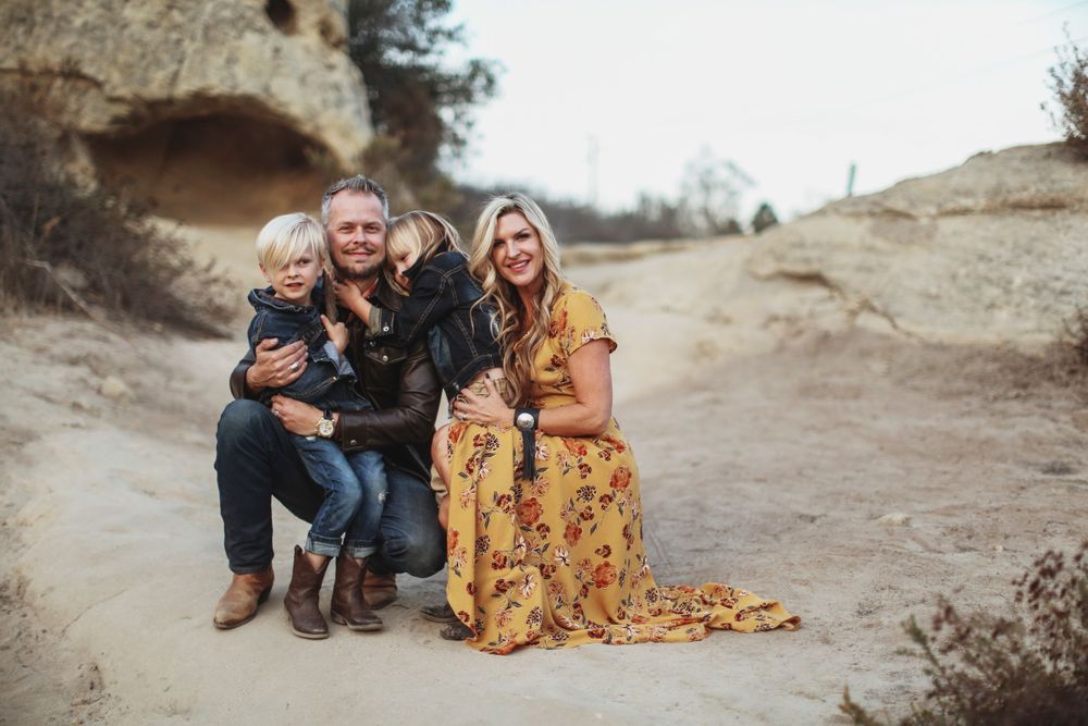 A group sits together outdoors on a sandy trail against a rocky backdrop during golden hour.