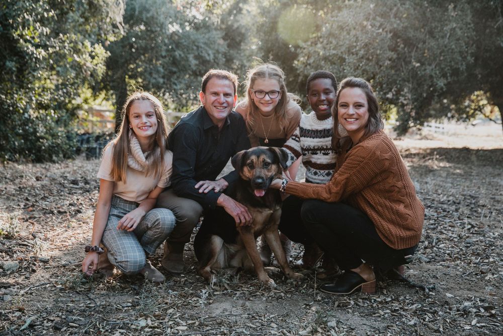 A group sits together outdoors with their happy Rottweiler mix dog on a sunny autumn day.