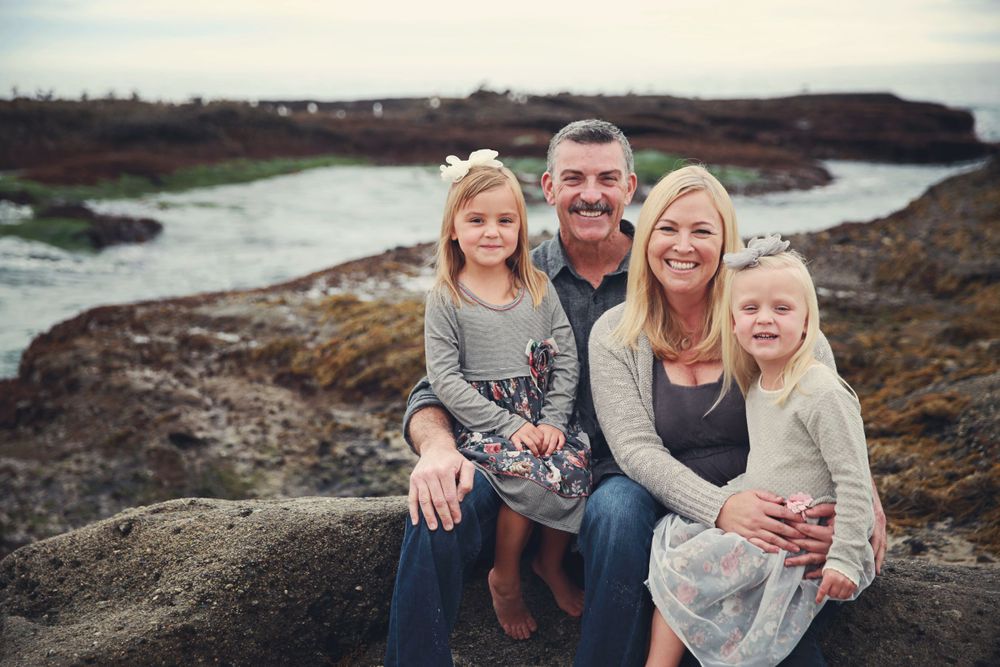 A family of four sits together on rocky cliffs overlooking a winding river during golden hour.