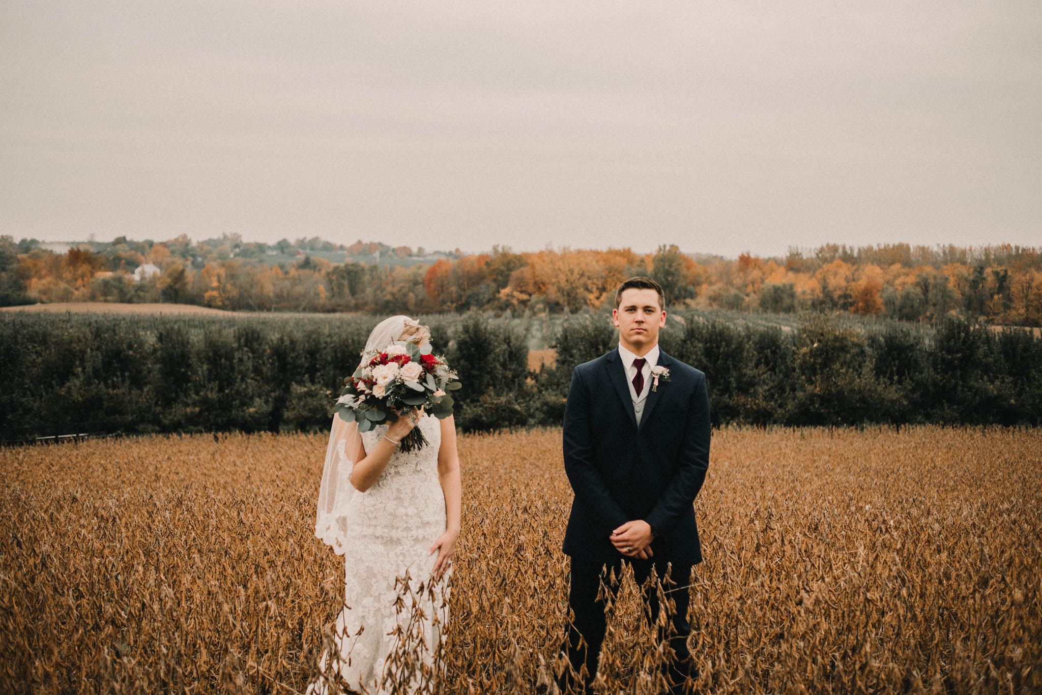 Wedding couple stands in a golden autumn field with rolling hills in the background.