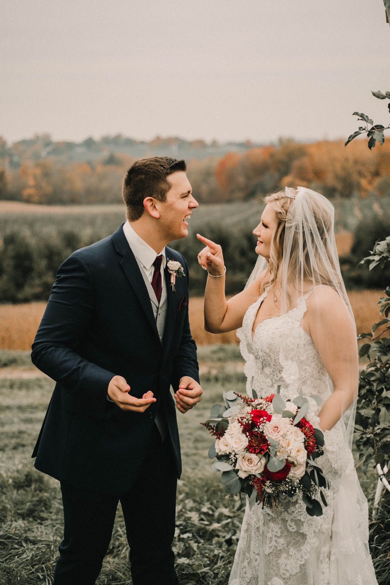 Playful candid moment between newlyweds with autumn foliage in background.