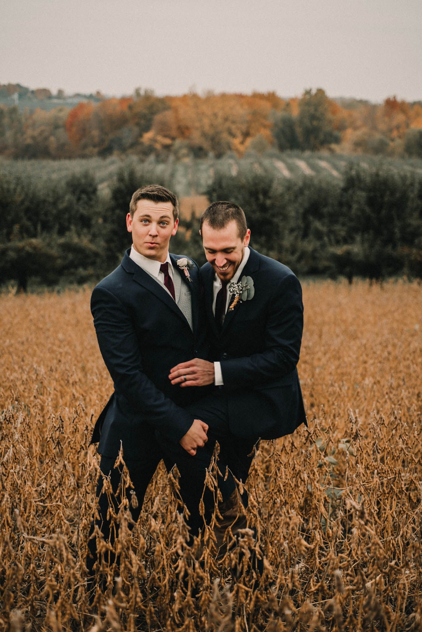 Two groomsmen share a candid moment in a golden autumn field.