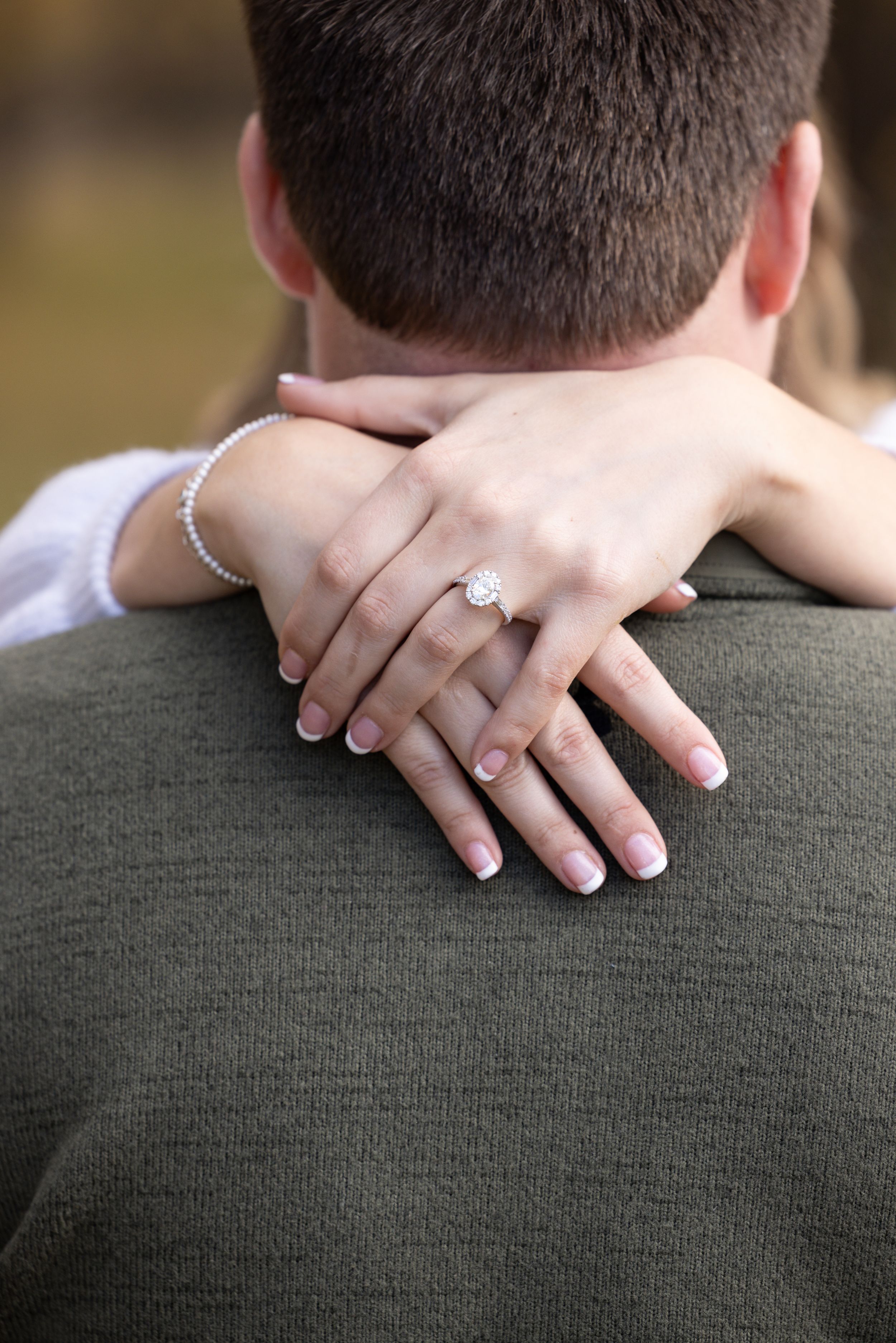 Close-up of hands with engagement rings embracing against a green sweater.