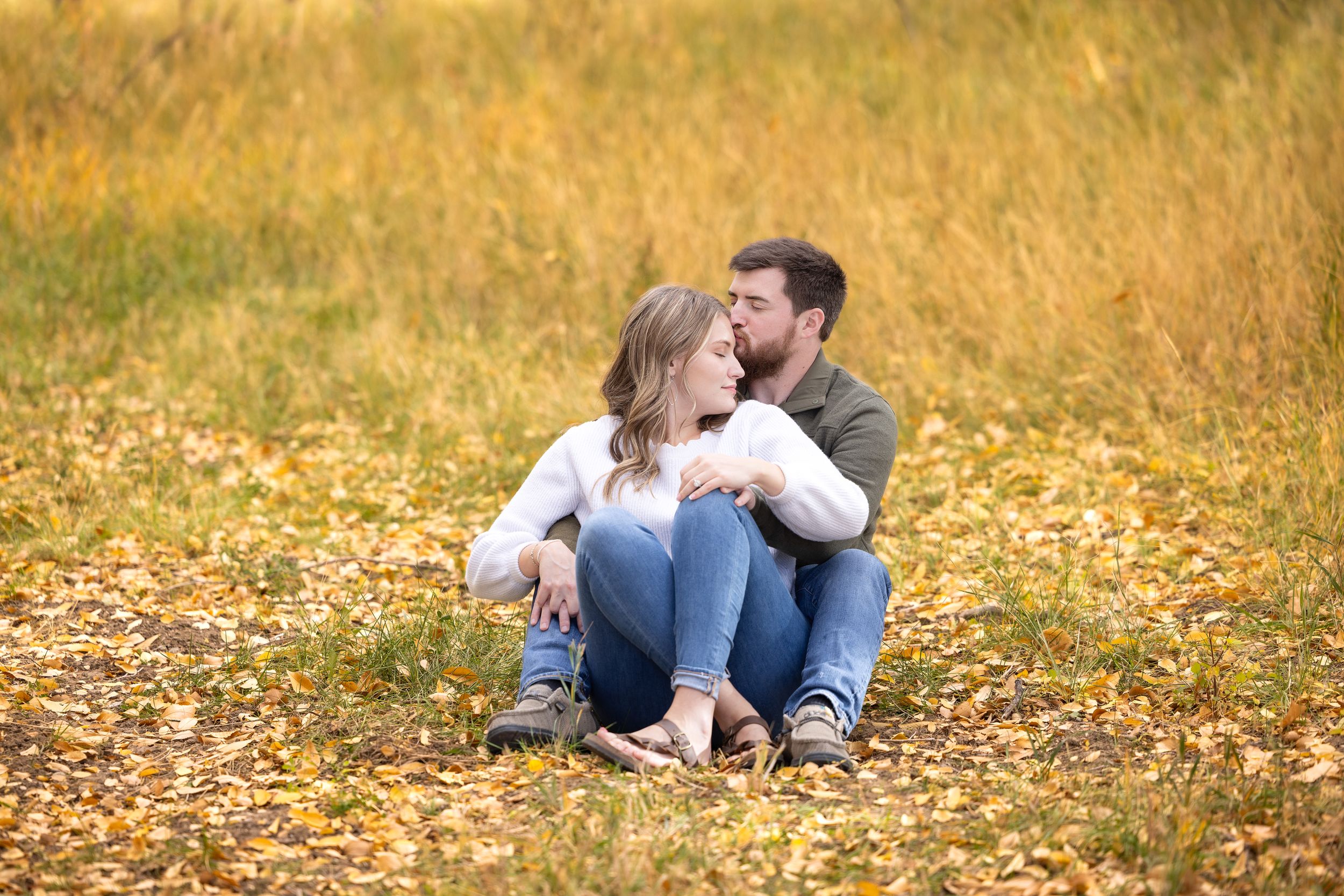 A couple sitting together on fallen autumn leaves in a golden field.