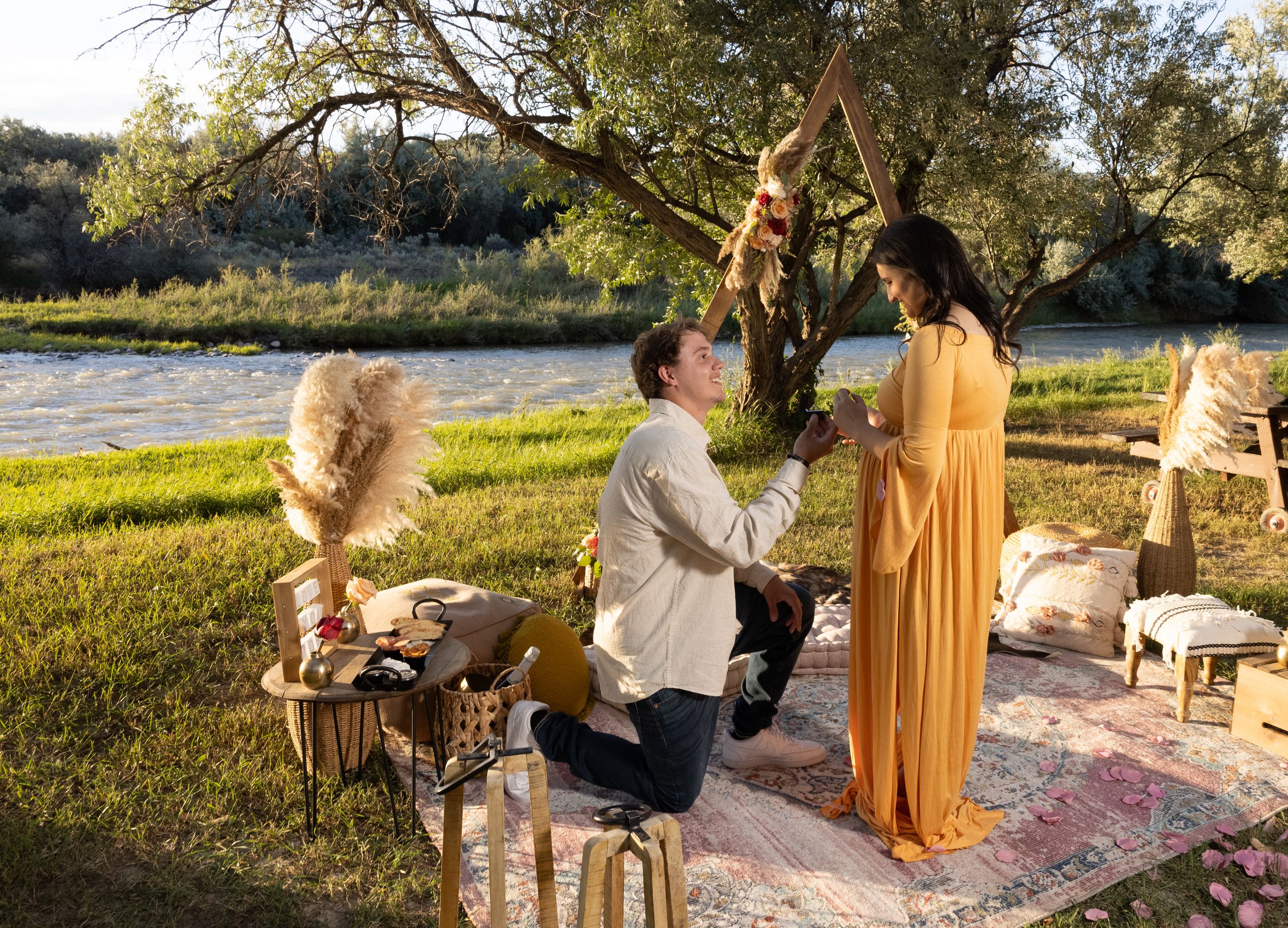 A romantic outdoor proposal setup near a river with decorative elements and furniture.