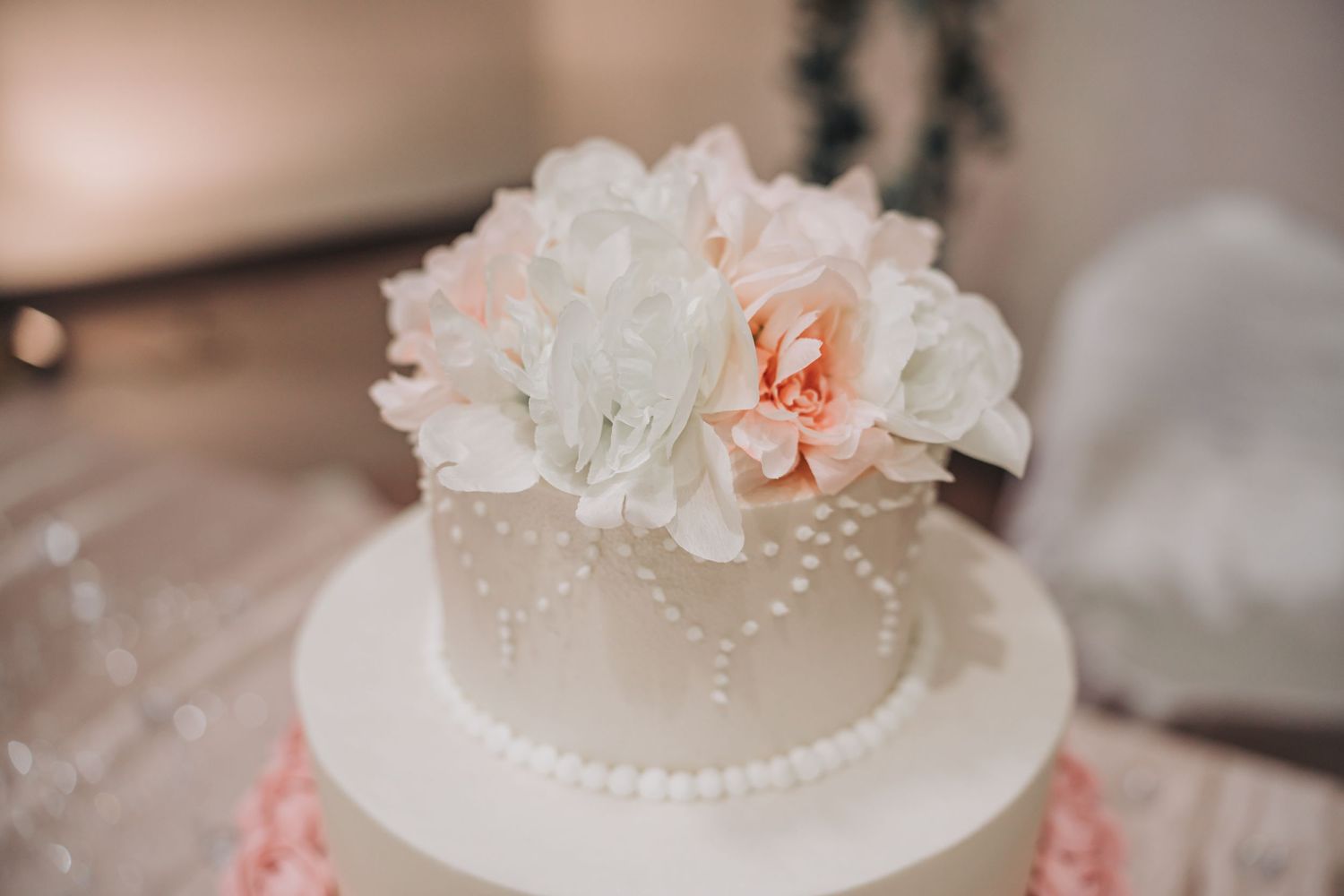 Elegant two-tier white wedding cake decorated with delicate pearl details and topped with soft pink and white flowers.
