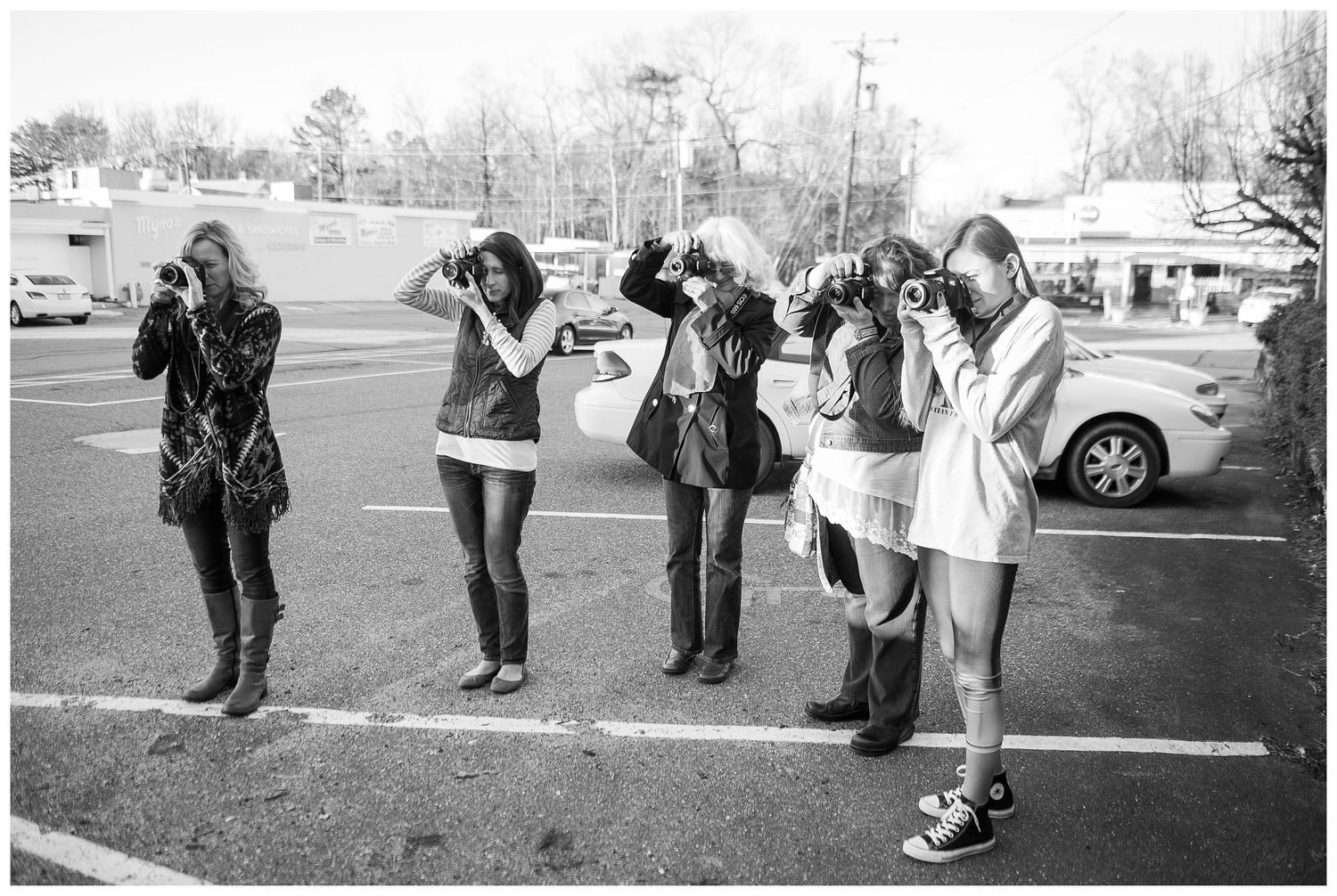 Black and white panoramic sequence of people gathered in a parking lot.