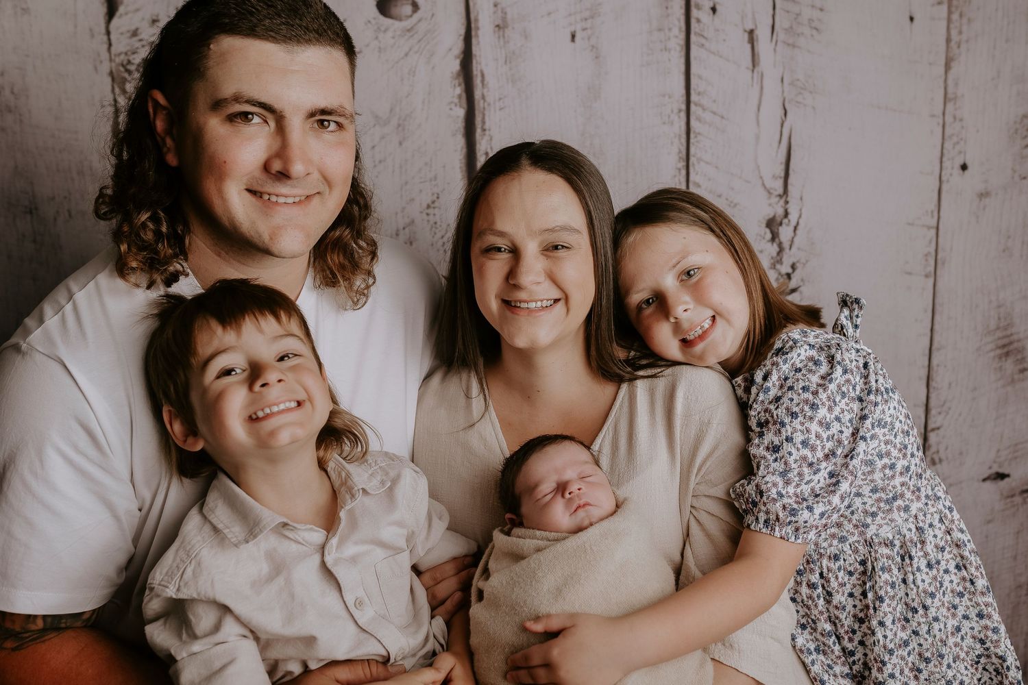 Natural light indoor family portrait session against rustic white backdrop.