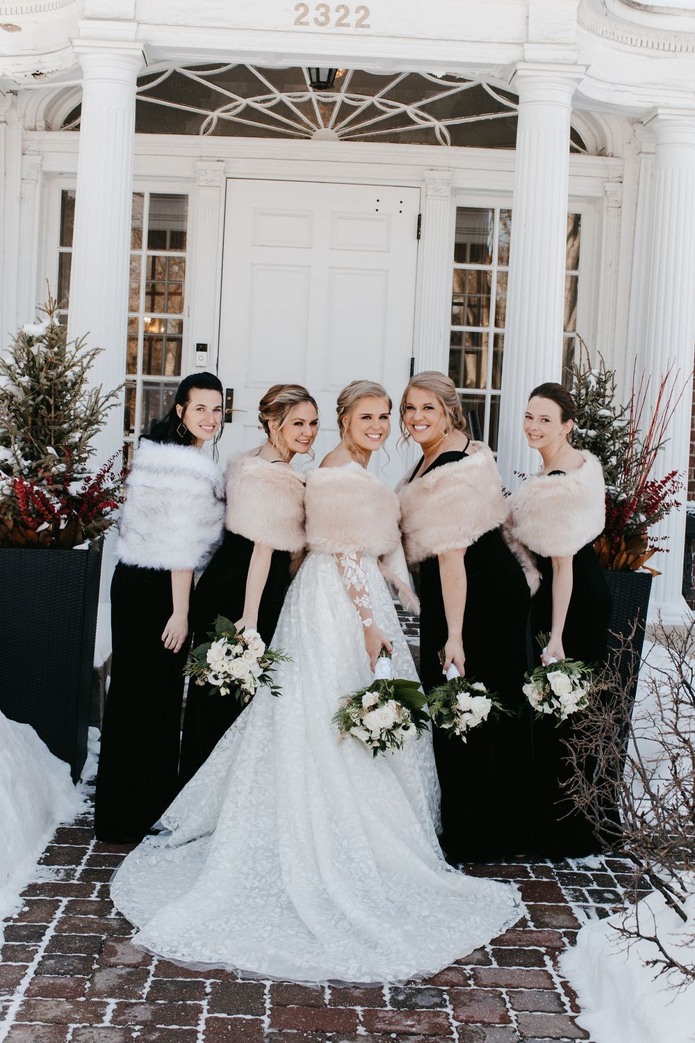 Bride in white gown with four bridesmaids in black dresses and fur shawls posing at entrance of building 2322.