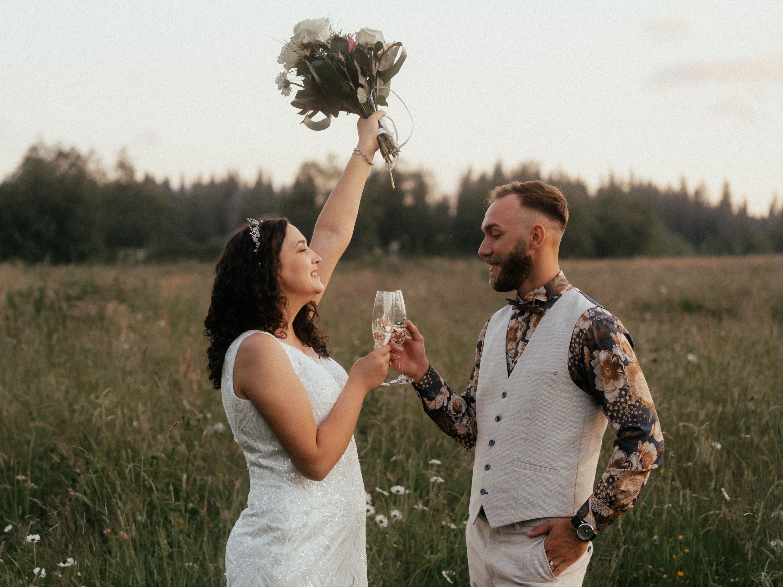 A joyful wedding couple stands in a green field