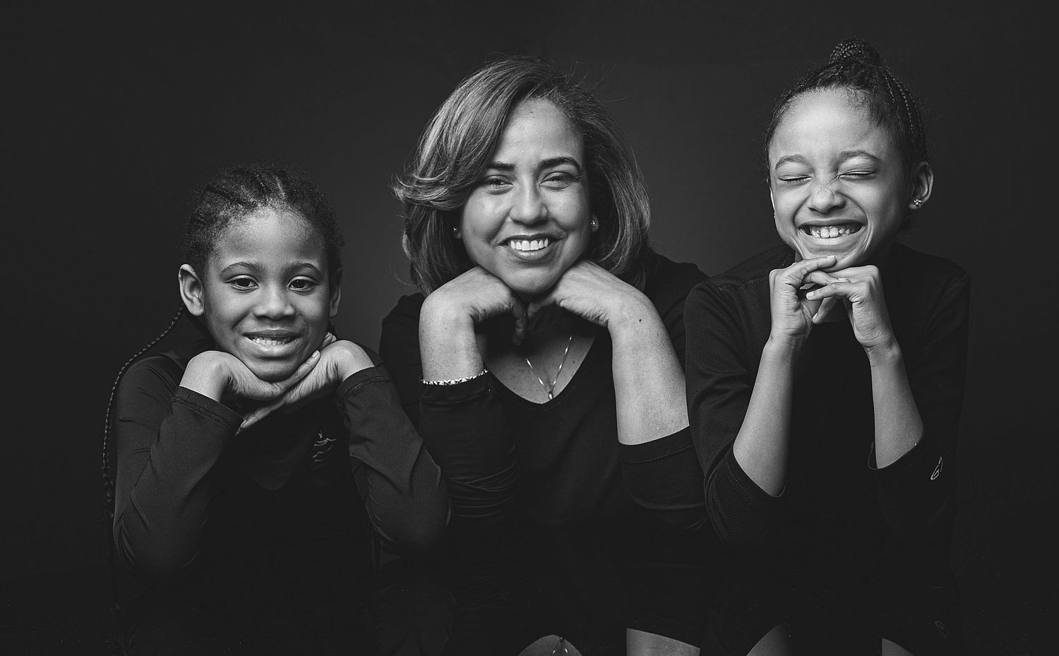 Black and white photo of a woman and two young girls smiling together in matching black tops.