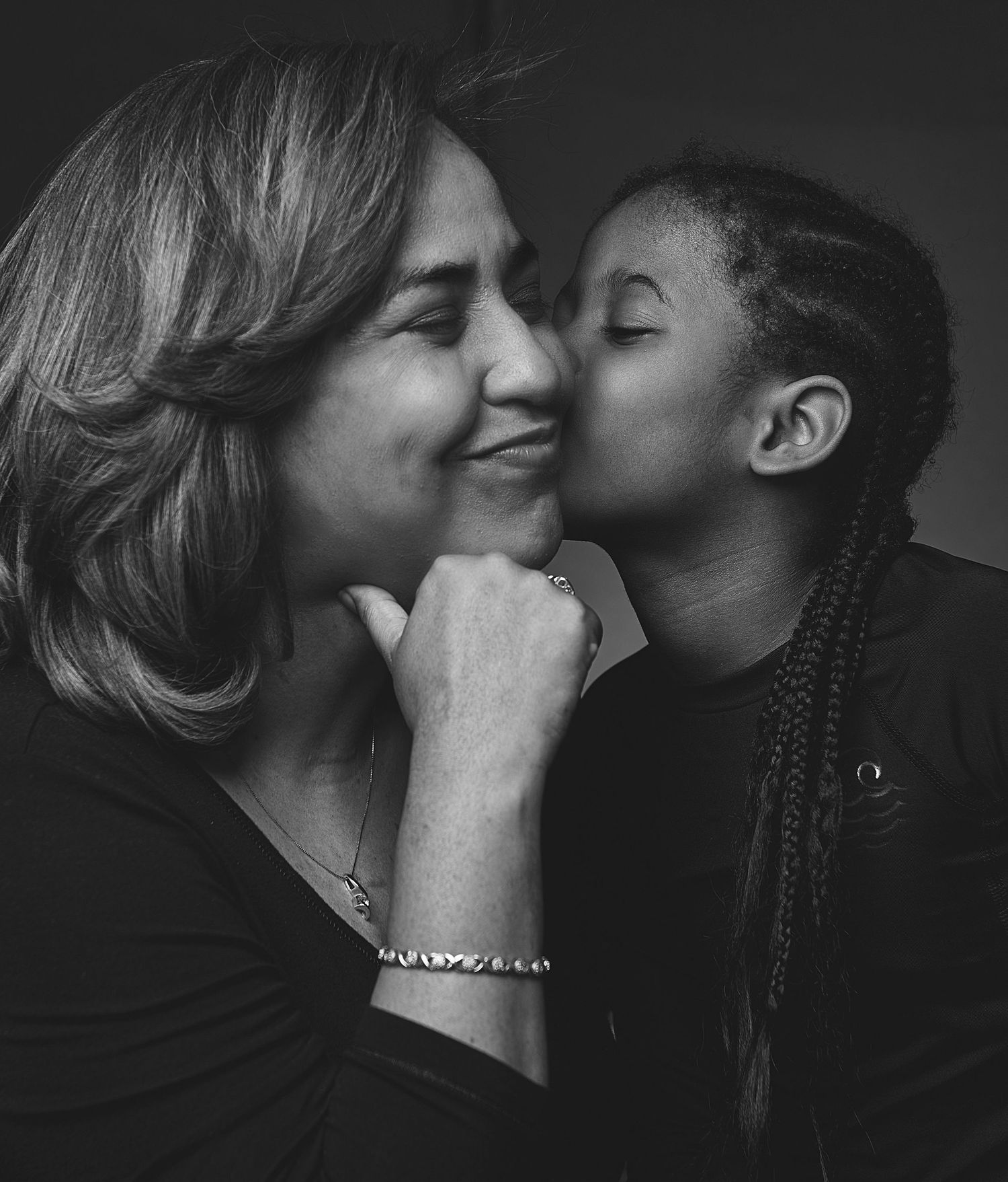 Black and white photo of a girl with braids kissing a smiling woman on the cheek.