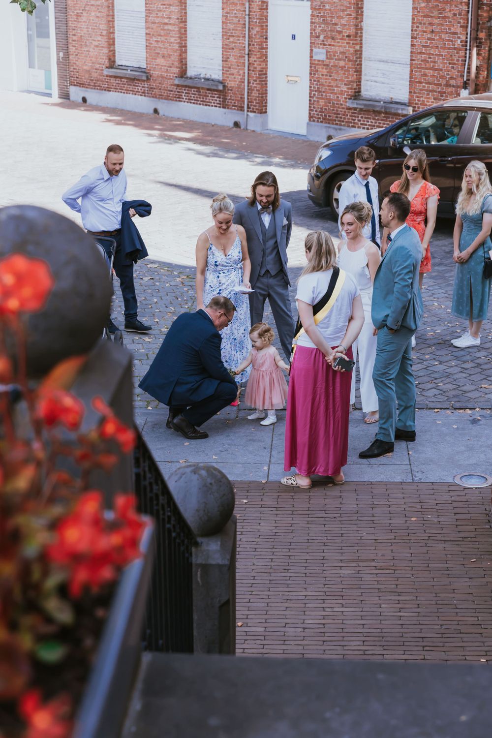 Wedding party gathered on cobblestone street with red brick building in background.