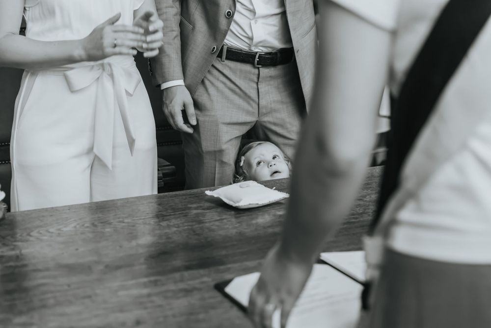 Black and white detail shot of hands resting on a wooden table during a ceremony.