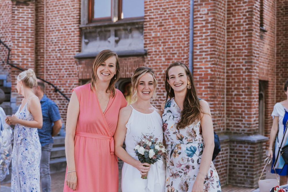 Three women pose together outside a brick building during a celebration.