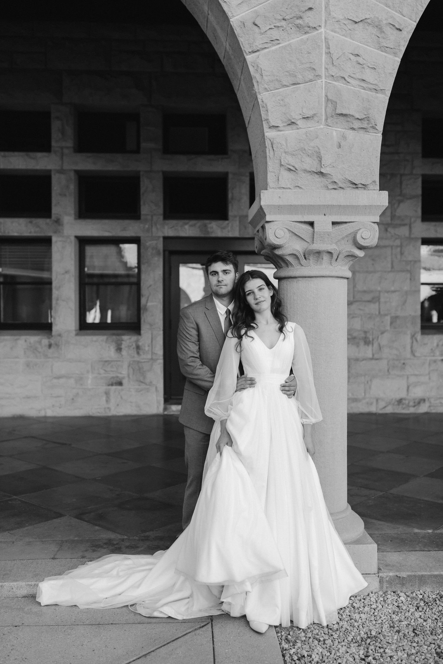 A classic wedding portrait featuring a couple standing by a decorative stone column in black and white.