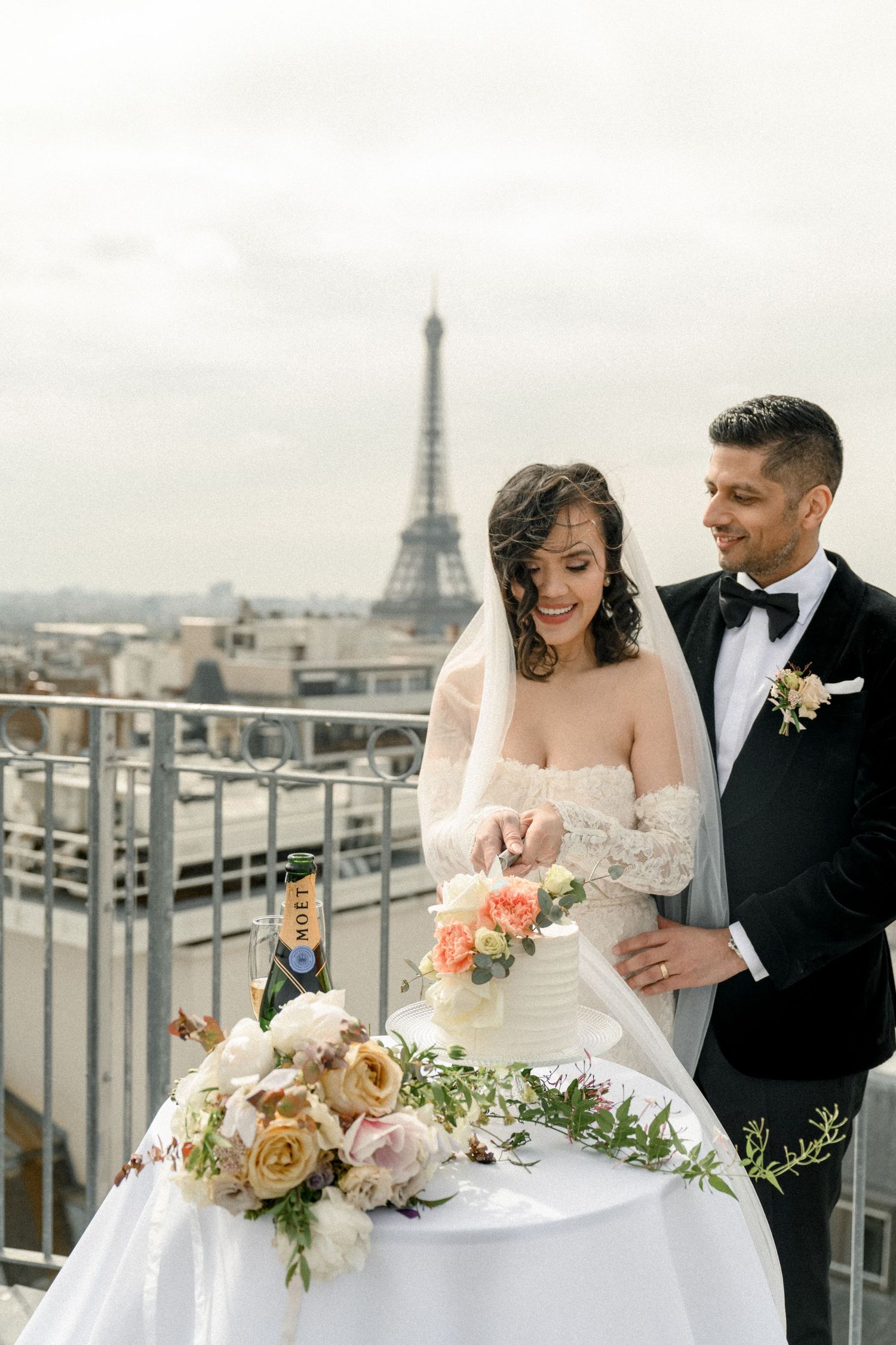 Wedding couple celebrates on a Parisian rooftop with flower arrangements and the Eiffel Tower in view.
