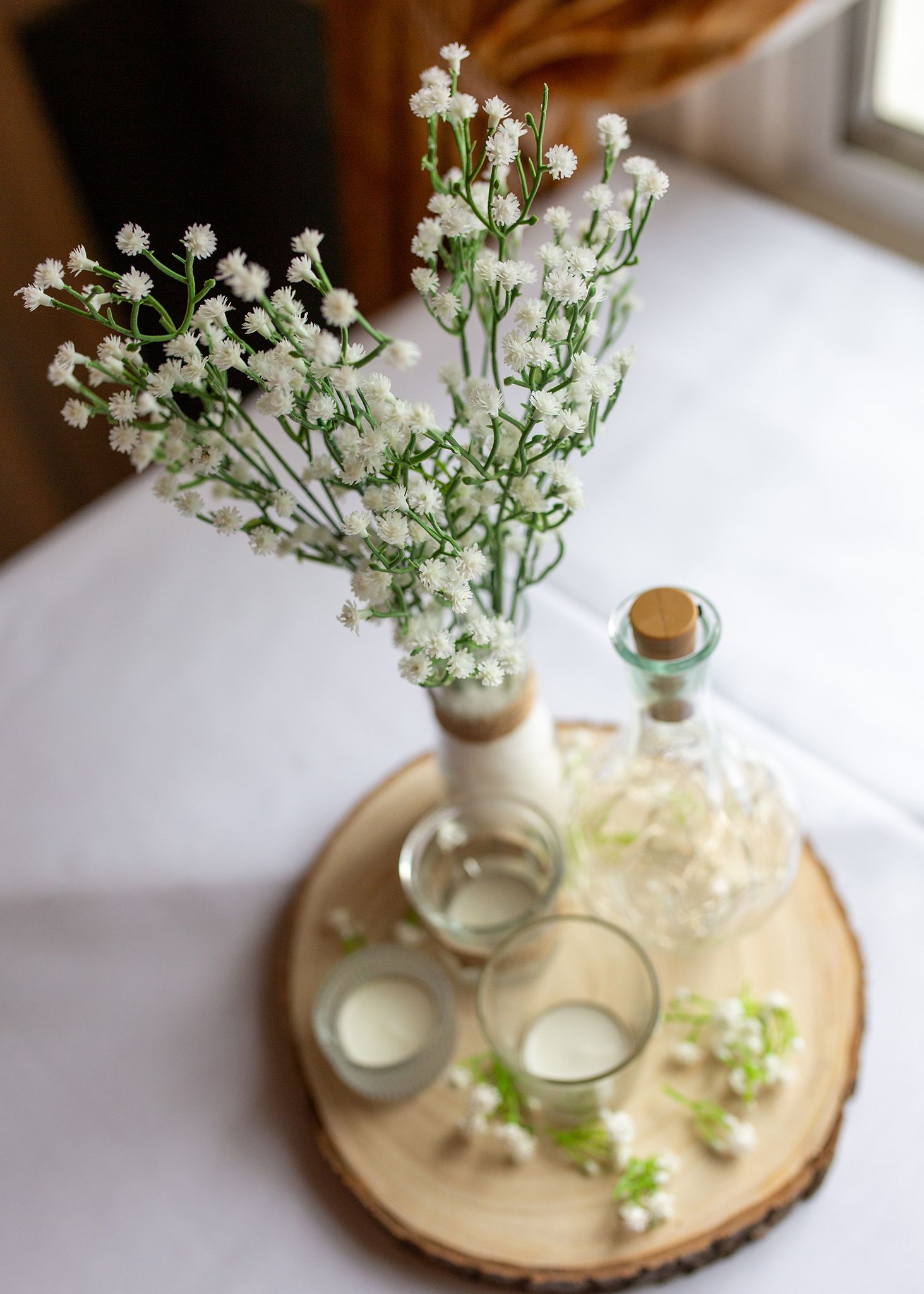 Baby's breath flowers in glass vases with candles arranged on wooden slice centerpiece.