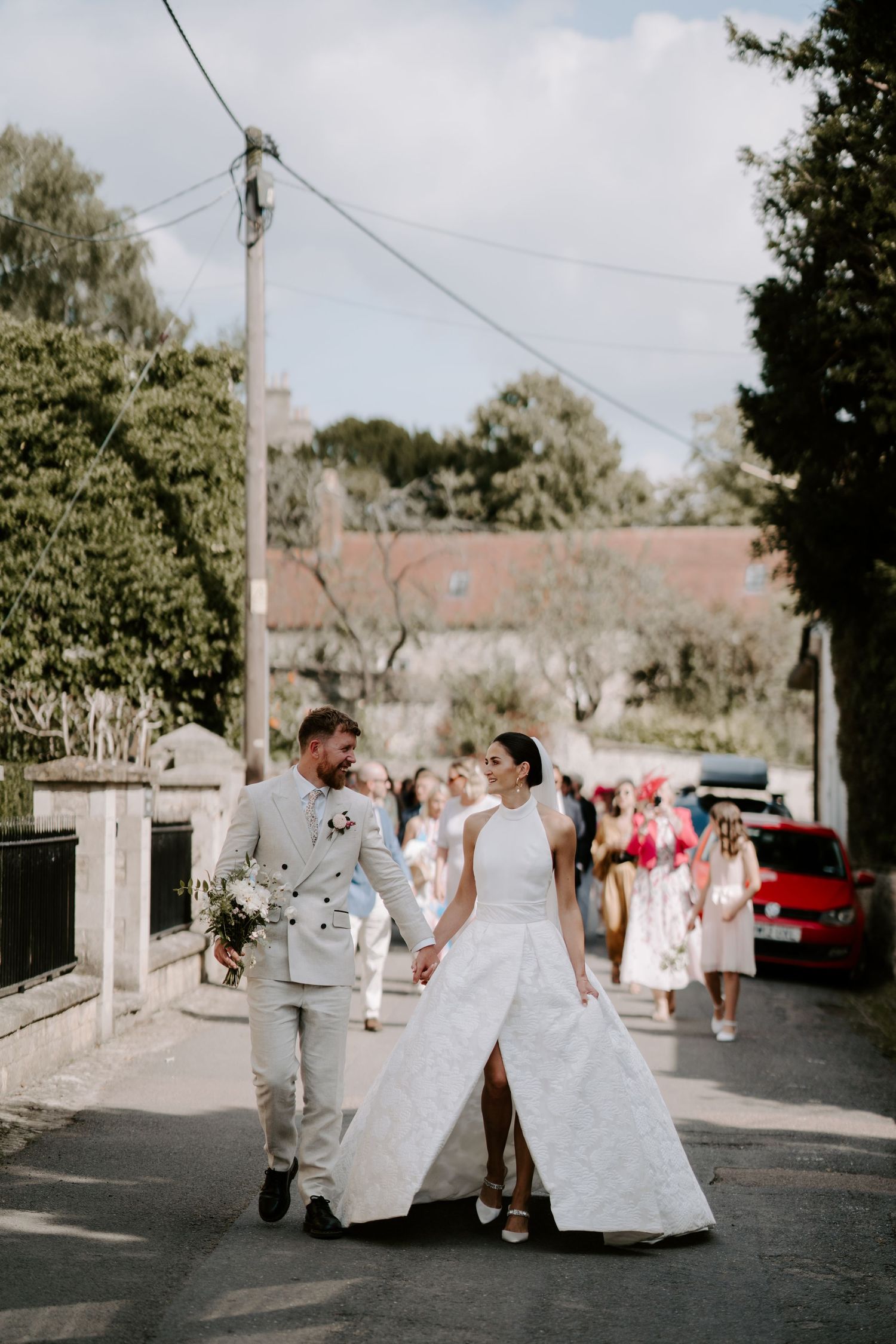 bride and groom walking through village followed by their wedding guests from st Nicholas church to marquee in islip in oxfordshire