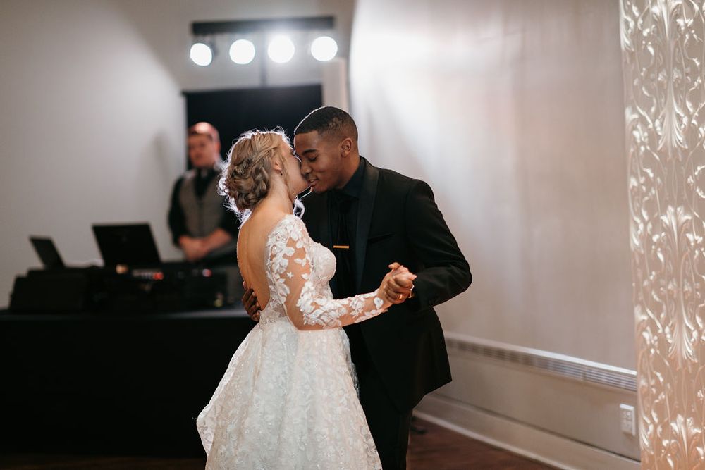 Bride and groom sharing their first dance with a DJ visible in the background at the wedding reception.