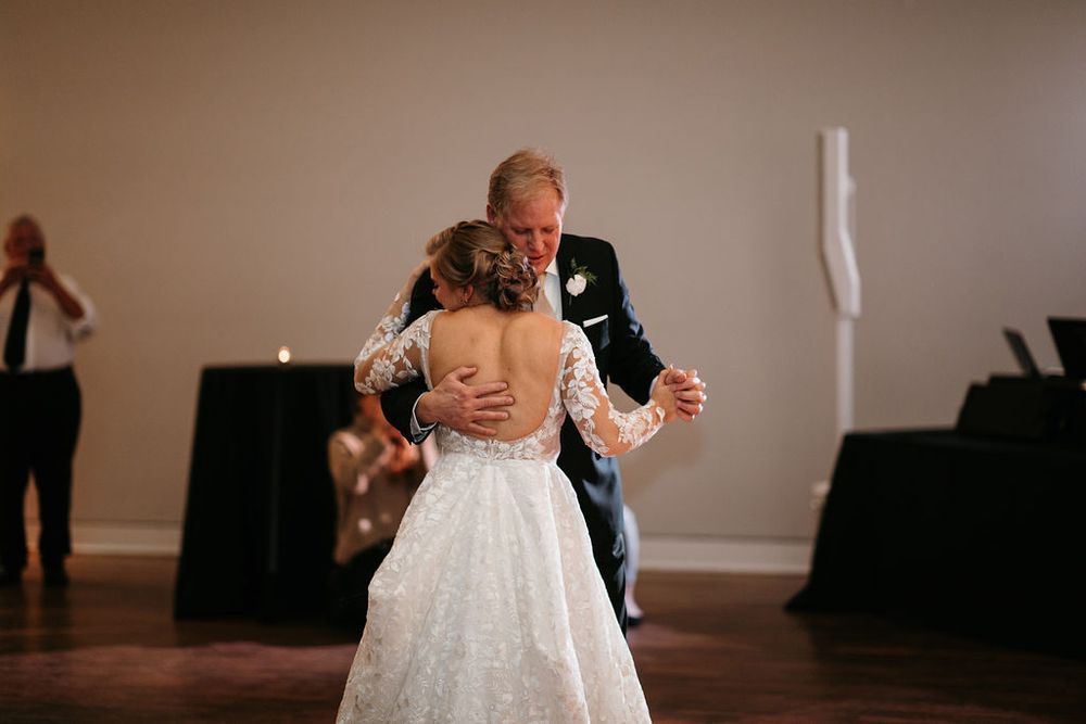 Bride in lace gown dances with her father during wedding reception father-daughter dance.