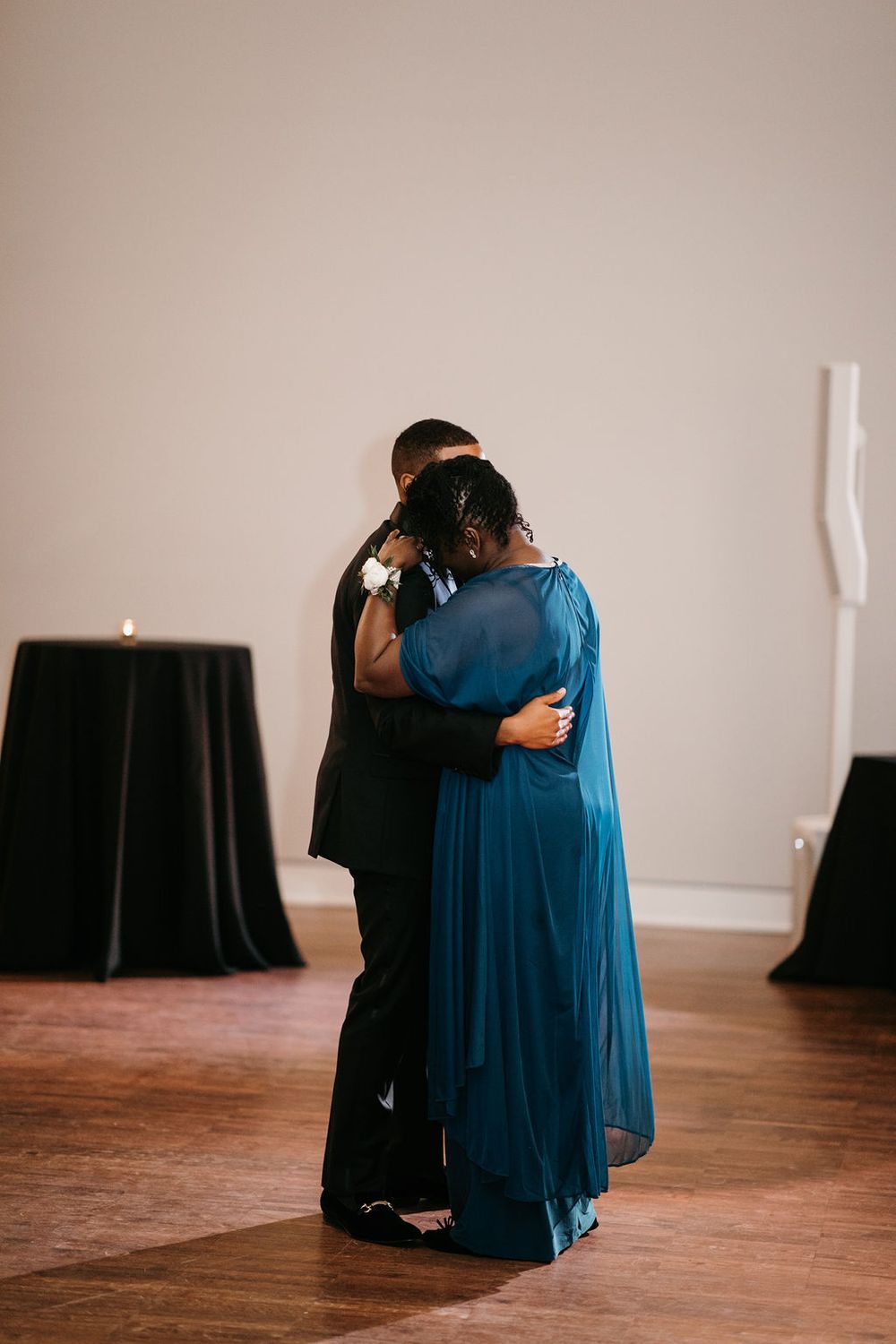 Groom and mother in teal gown share a warm embrace during mother-son dance.