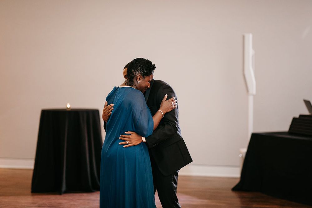 Groom and mother in teal dress share a heartfelt hug during wedding reception dance.