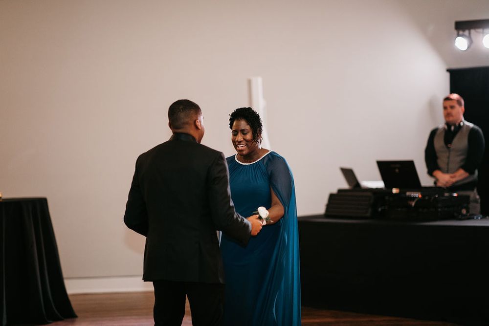 Groom and smiling mother in teal dress share a joyful moment on the dance floor.