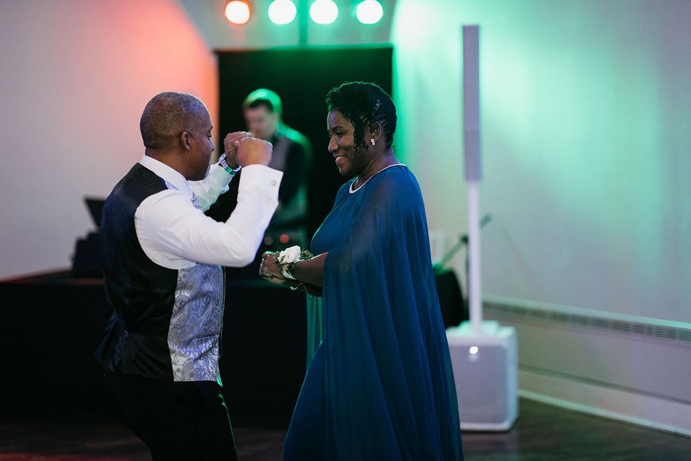 Couple shares an elegant dance at a wedding reception with colorful stage lighting in the background.