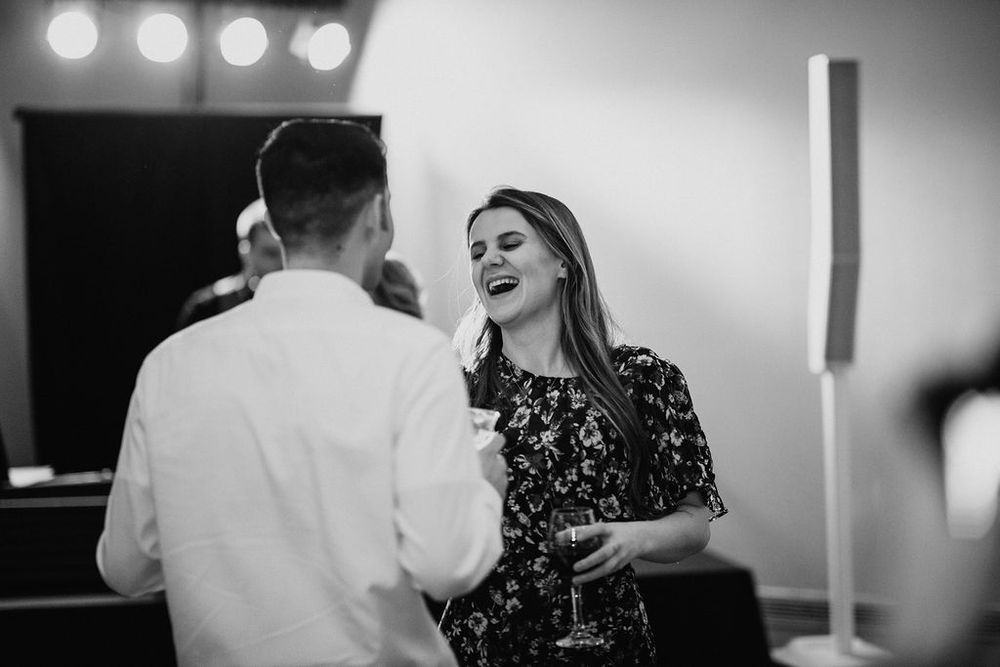 Black and white photo of woman in floral dress laughing while holding a champagne glass at wedding.
