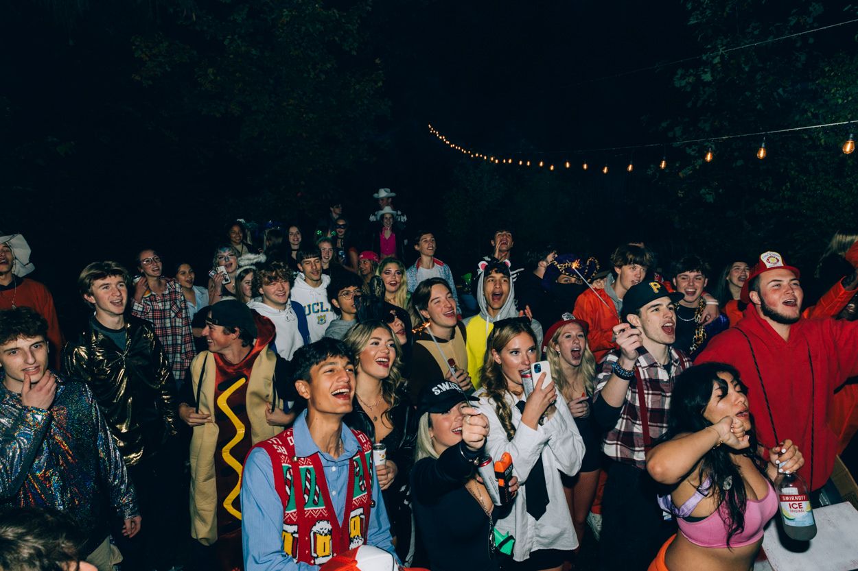 Festive crowd in Halloween costumes gathered outdoors under string lights.