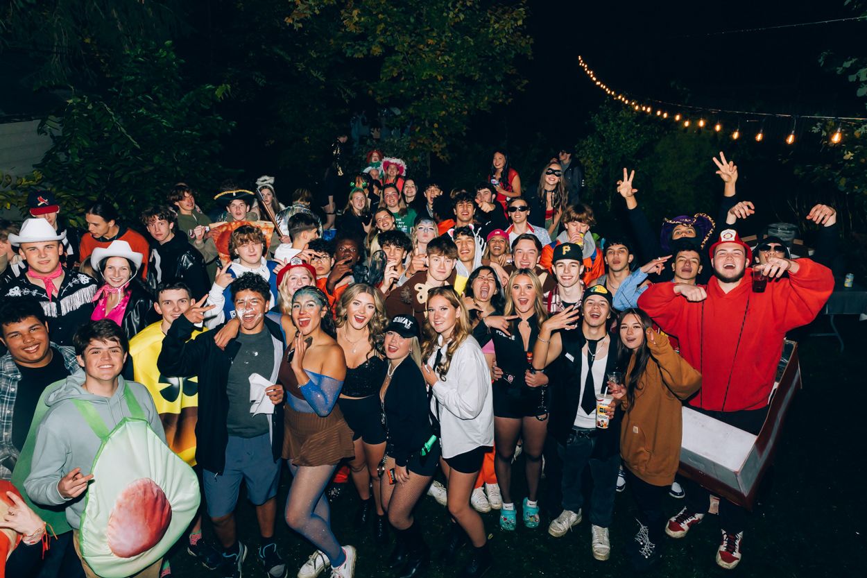 Large crowd of party attendees gathered outdoors at night under string lights.