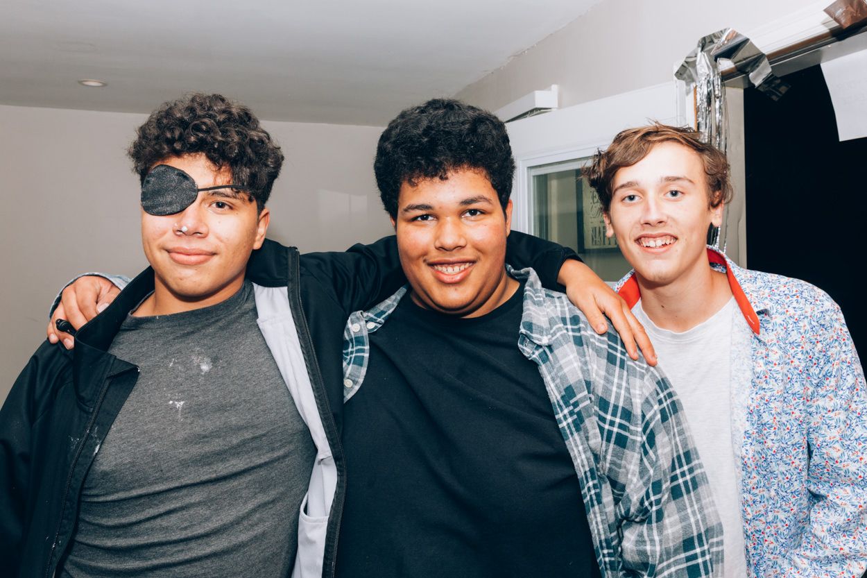 Three friends smiling and posing together indoors against a white wall.