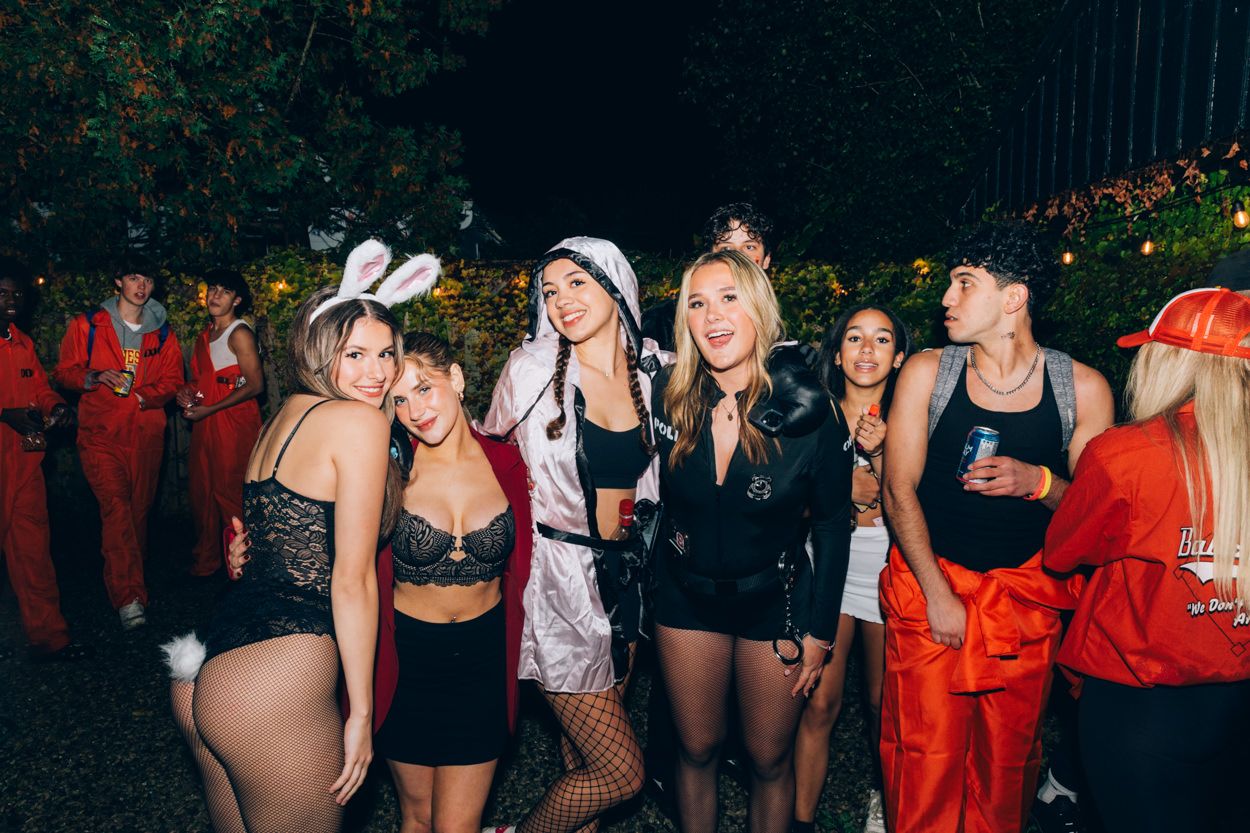 Group of partygoers in dark clothing and costumes gathered outdoors at night.