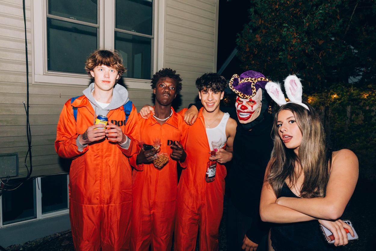 Group of young people in orange jumpsuits and costumes posing together at a nighttime party.