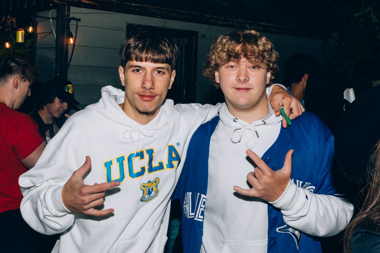 Two people wearing university sweatshirts pose together at nighttime party.