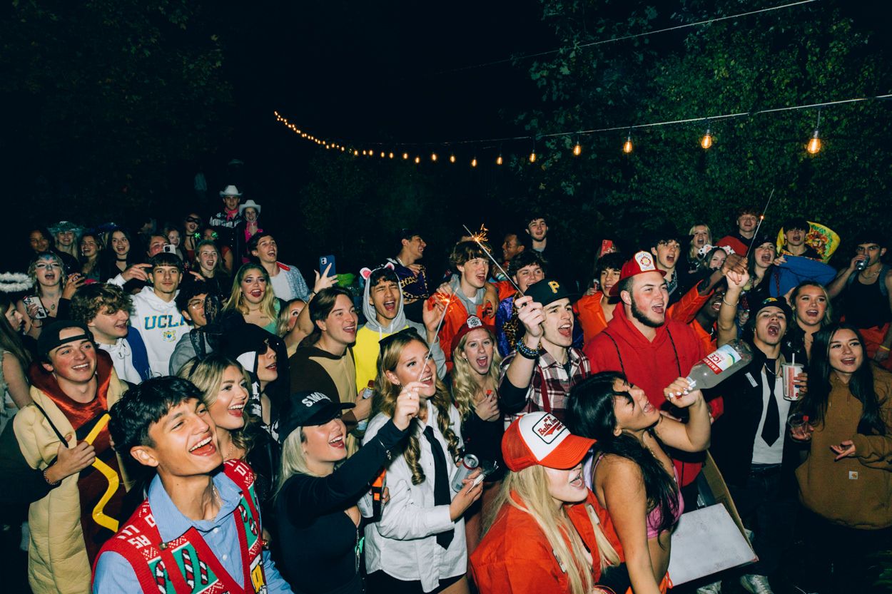 Large crowd of costumed partygoers dancing under string lights at night.