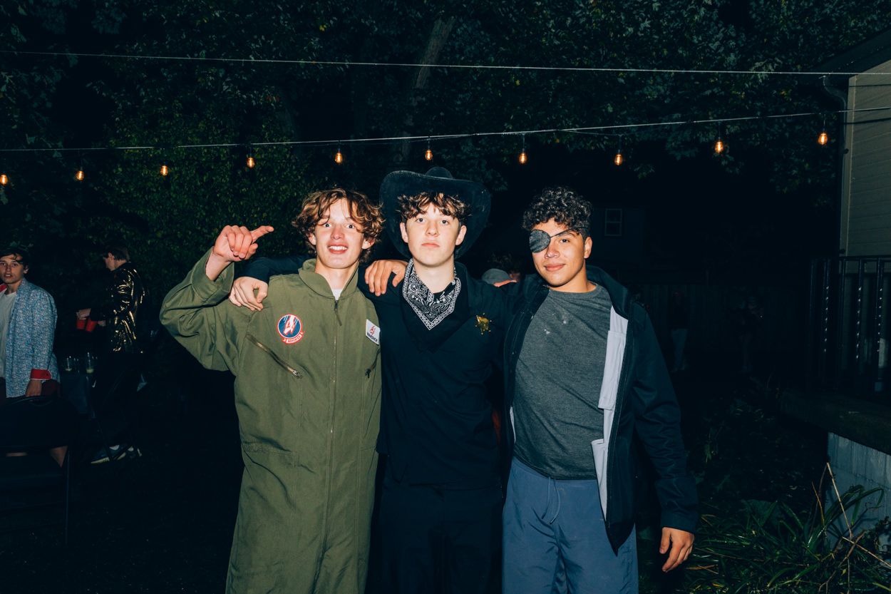 Three friends pose together under string lights at nighttime outdoor party.