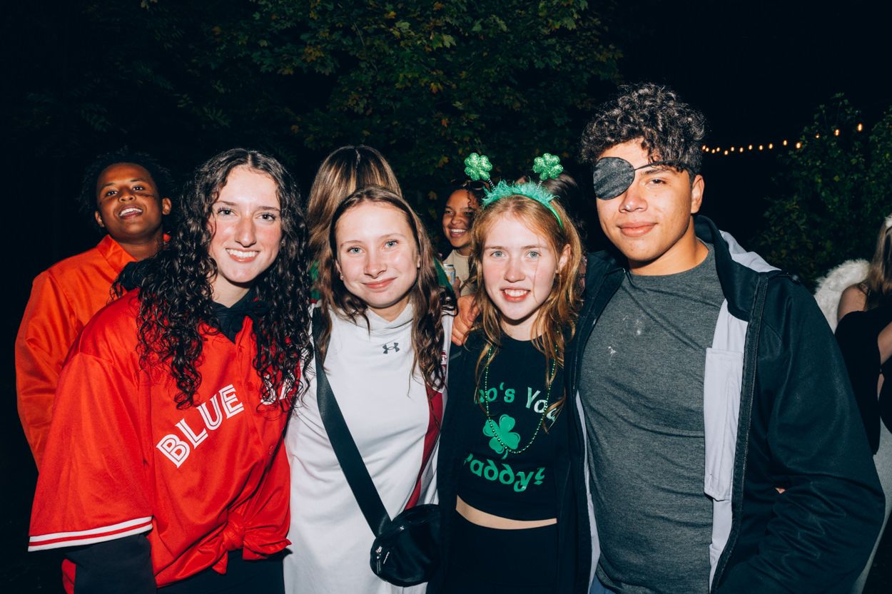 Group of friends in casual attire pose together at outdoor nighttime gathering.