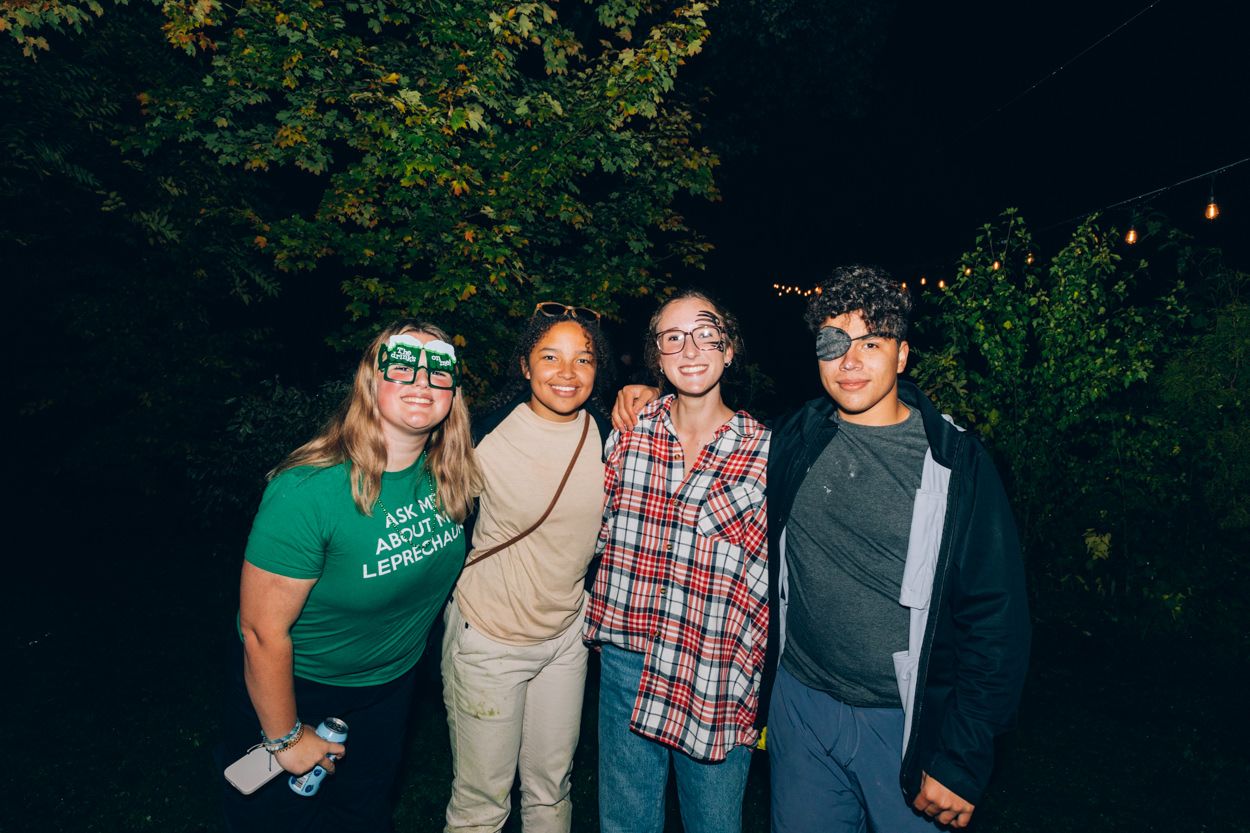 Friends pose together outdoors at night with string lights visible in background.