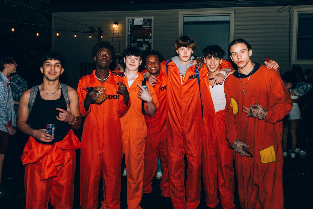 Group wearing matching orange jumpsuits poses together at nighttime party.