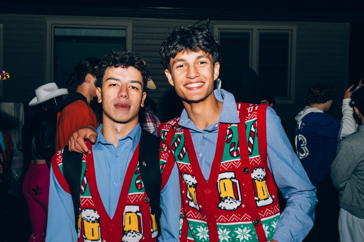 Two people wearing matching Christmas sweater vests smile together at holiday party.